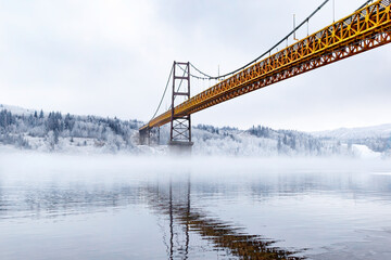Steel and concrete bridge across the foggy river in winter.