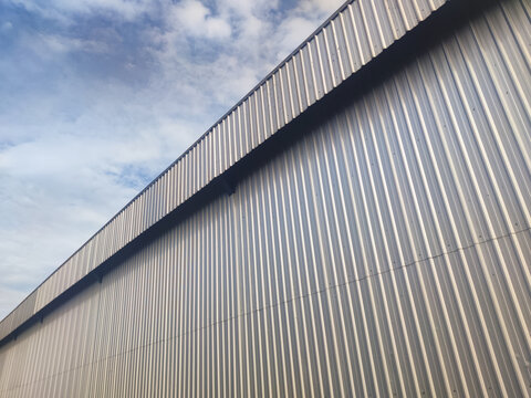 A diagonal perspective of corrugated steel siding against a bright sky, showcasing industrial geometry and contrasting tones ideal for architectural or texture themes