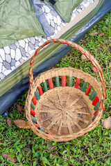 Empty woven basket with red and green slats beside tent in outdoor setting.