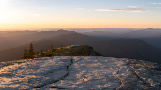 Panoramic view of a serene mountain landscape at sunset with a rocky foreground and distant hills under a warm, orange-blue sky.