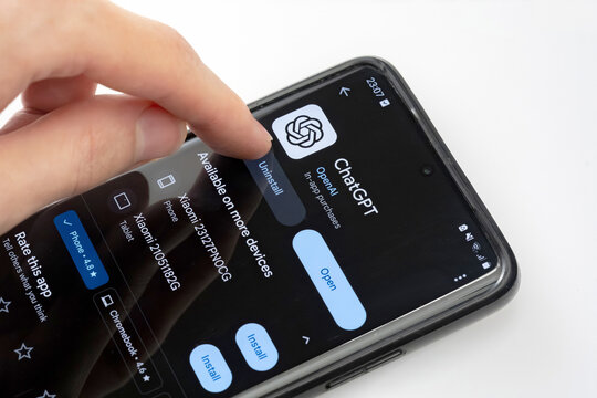 Person uninstalling ChatGPT OpenAI chatbot app from a smartphone, hand pressing uninstall button closeup. AI trend over abstract concept, deleting removing mobile application software, one person