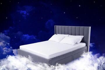 Large bed on fluffy clouds in starry night sky