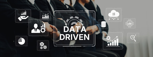 Business professionals engage in a discussion about data-driven strategies, surrounded by digital icons representing analytics and growth, in a modern office setting. Trope