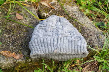 Gray knitted beanie on mossy stone surface surrounded by grass and leaves outdoors.