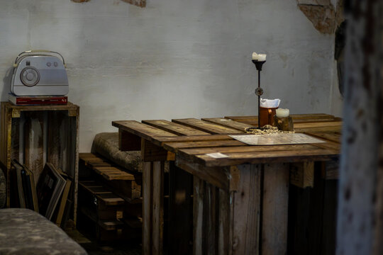 Cozy rustic interior of a cafe or bar, featuring a wooden pallet table, comfortable seating, ambient candlelight, and a vintage radio on a crate with books. Warm lighting, inviting atmosphere - Powered by Adobe