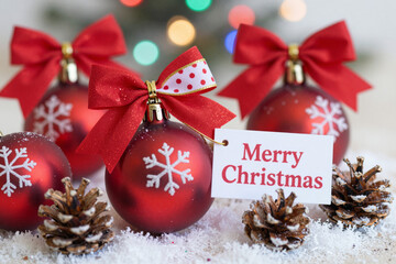 Bright red Christmas decorations, including ornate baubles, a "Merry Christmas" tag, and natural pinecones, convey warm holiday greetings