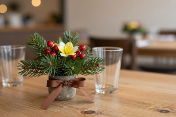 Charming festive centerpiece with pine, berries, and a vibrant yellow flower adorning a rustic wooden table in a cozy cafe setting