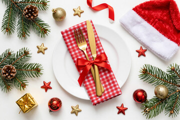 Christmas table setting with golden cutlery, Santa hat, pine branches, and festive decorations on white background, perfect for holiday dining