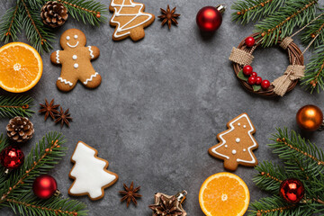 Festive Christmas flat lay border with gingerbread cookies, vibrant orange slices, fresh pine branches, and classic holiday ornaments on a dark textured background