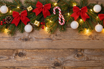 Festive Christmas Garland Adorned with Red Bows, White Ornaments, and Warm Lights on a Rustic Wooden Background, Evoking Holiday Cheer and Traditional Seasonal Spirit
