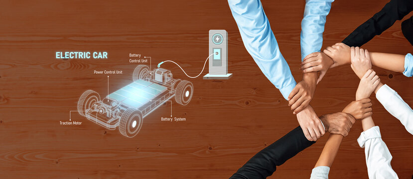 Hands come together to symbolize collaboration in electric car technology, featuring a design and battery charging setup against a wooden background. Trope