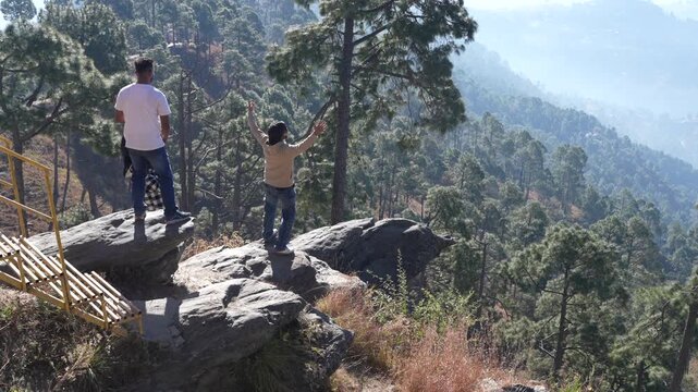 Group of friends (Non-Identifiable) standing on a rocky cliff edge at Kasar Devi Almora looking at scenic Himalayan mountain view and pine forest, Uttarakhand Tourism 4K