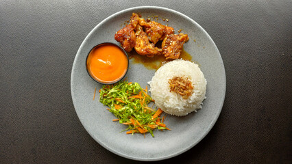 Overhead shot of crispy glazed chicken served with white rice, fresh shredded salad, and dipping...