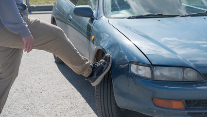Caucasian man tries to fix damage to car body with his foot. 