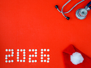 2026 Happy New Year banner for health care and medical concept. Number 2026 made from tablets, stethoscope and Santa hat on a red background. View from above flat lay. Medical concept. Copy space