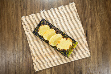 Four grilled flatbreads or pancakes on a black plate with bamboo mat and wooden table.