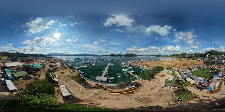 Wide aerial view of Lualhati Park plaza featuring I am Coron sign and harbor filled with tourist outrigger boats under blue sky
