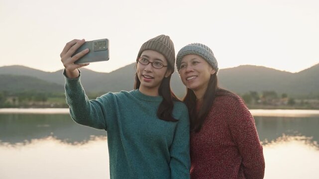 Family.Asian mother daughter taking photo selfie together at camping outdoor river at sunset