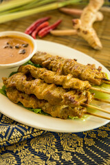 Grilled satay skewers served with peanut sauce and lettuce, garnished with chili and herbs.