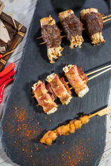 Grilled skewers with beef, bacon, chicken, and enoki mushrooms, garnished with chili powder.