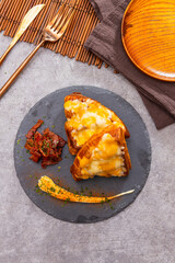 Croissants topped with cheese and bacon, served with creamy herb sauce on slate plate.