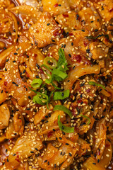 Korean-style stir-fried pork with kimchi in red chili sauce, garnished with sesame seeds and green onions.