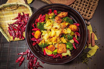 Stir-fried tofu, potato, broccoli, and chili in a dark bowl with sesame seeds and rustic props.