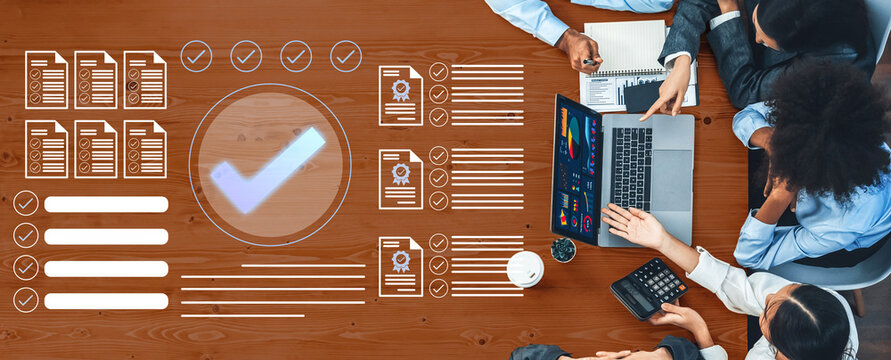 A diverse business team collaborates around a table, analyzing data and reviewing documents while utilizing a laptop, showcasing teamwork and productivity in action. Gantry - Powered by Adobe