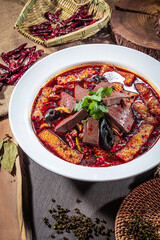 Spicy Sichuan-style hot pot with tofu skin, congealed blood, mushrooms, and chili oil, styled with rustic props.