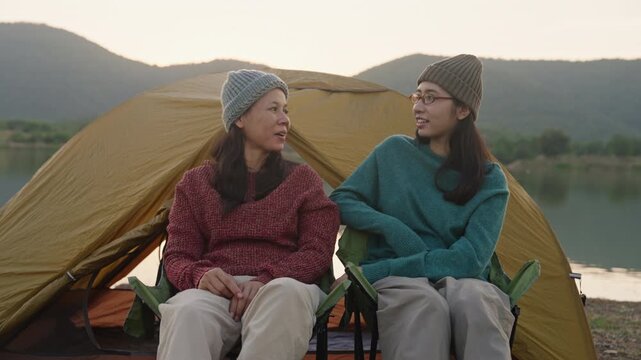 Camping.Asian mother daughter talking happy together at campsite outdoor river at sunset
