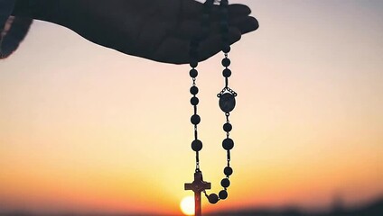 Silhouette of Hand Holding Catholic Rosary Beads with Cross Against Golden Sunset