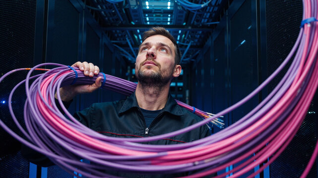 It technician with cables in server room looking up at the network infrastructure and equipment racks