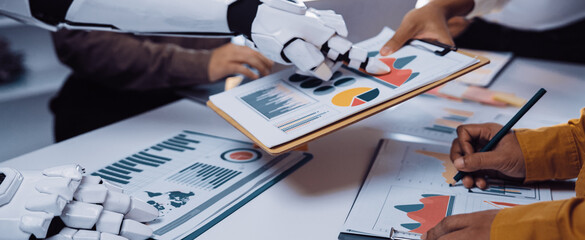 A futuristic office scene showcasing collaboration between a robot and humans. They analyze data charts and graphs, highlighting teamwork and innovation in the workspace.Noogenesis