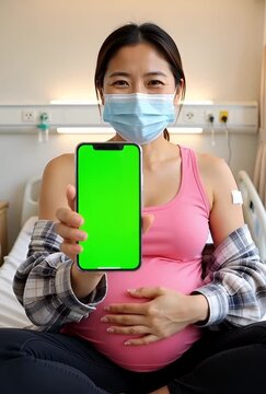 Expectant mother shows green screen smartphone while in hospital bed, ready for your app or ad, she's wearing a mask and has a bandage after vaccine