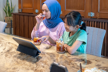 Indonesian muslim woman and a child are watching a movie through a tablet in front of them in a cafe