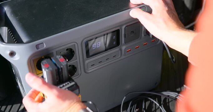 Close-up of a hand plugging a USB cable into a portable power station. The device is simultaneously charging drone batteries, perfect for mobile creators and road trips