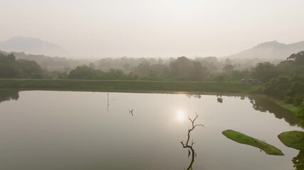 Backlit Sri Lanka lake with small grassy islets and bright sun glitter on the surface near wooded banks.