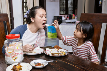Asian woman and a child are eating in dinning table. Daughter feeding her mother while eating together.