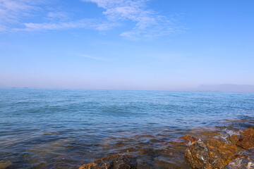 Calm blue sea landscape with rocky shore under clear bright sky
