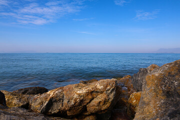 Coastal rocks and rippling blue sea under a clear sky background.