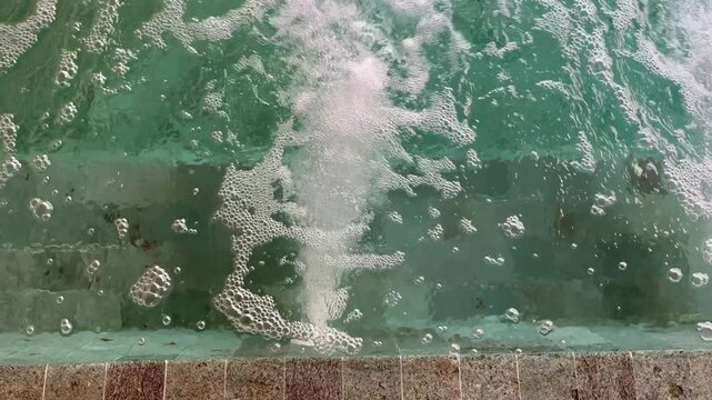 A lively pool surface with bubbling water jets creating swirling foam and ripples, resembling a jacuzzi effect, captured close-up to highlight texture, movement, and sparkling turquoise tones