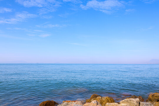 Calm blue water and sky seascape with rocky shoreline and wide copy space.