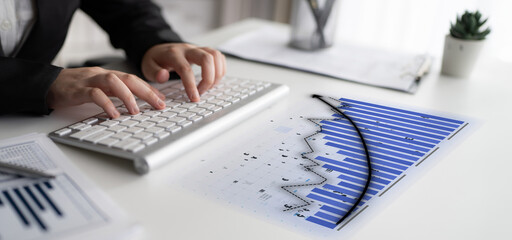A business professional focuses on analyzing financial data at a modern office desk. The scene features a keyboard, charts, and a small plant, symbolizing productivity and innovation. Impute
