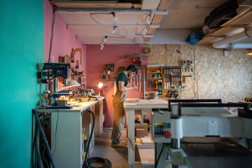 Man carpenter works on private order at table with tools in spacious workshop filled with equipment and materials perfect for manufacturing unique furniture items, small business and craft products.