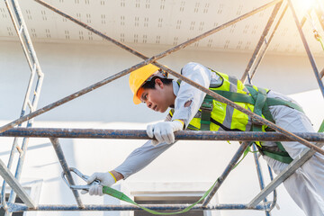 Construction worker in safety gear working on scaffolding during daylight, focusing on securing safety harness, representing construction and safety practices