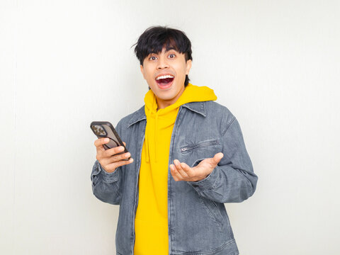Happy young Asian man holding a smartphone with an excited expression, perfect for technology ads, digital services, online apps, mobile innovation, and modern communication concepts.