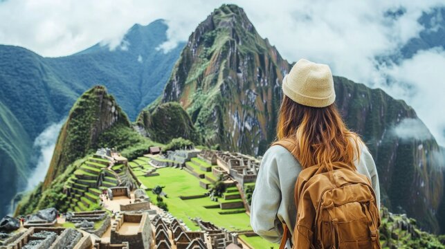 A woman in a hat and backpack admires the ancient Incan ruins of Machu Picchu, with lush green mountains in the background. - Powered by Adobe