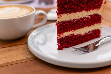 Primer plano macro de la textura lateral de una torta Red Velvet, mostrando las capas de bizcocho rojo esponjoso y relleno de queso crema. Café desenfocado al fondo.