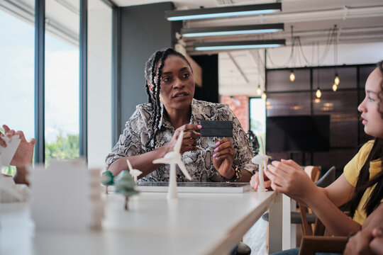 Black female teacher teaches and instructs primary girls group students, clean energy lesson at learning table in science classroom, discusses experiment knowledge for children of elementary school. - Powered by Adobe