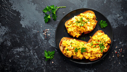 Two pieces of scrambled egg toast with parsley on a dark textured plate scrambled eggs